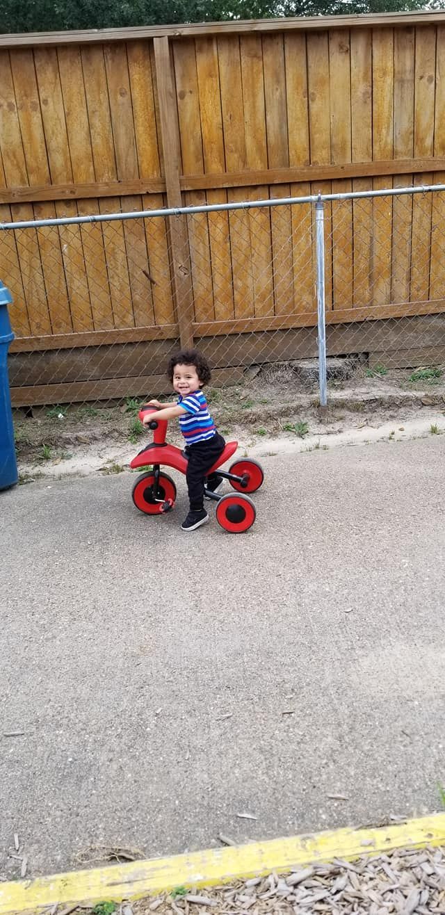 Toddler riding a red tricycle in a paved yard
