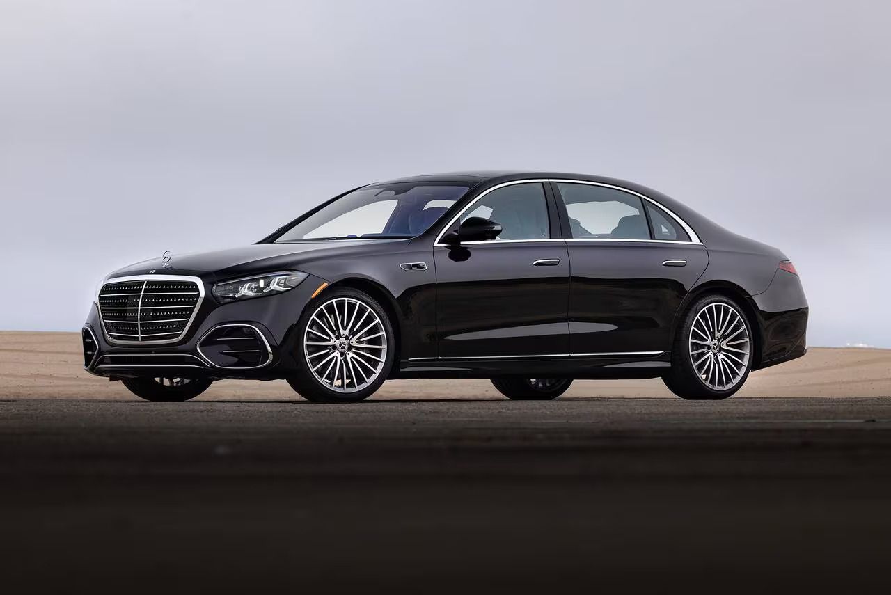 Black luxury sedan parked on a road against a cloudy sky backdrop