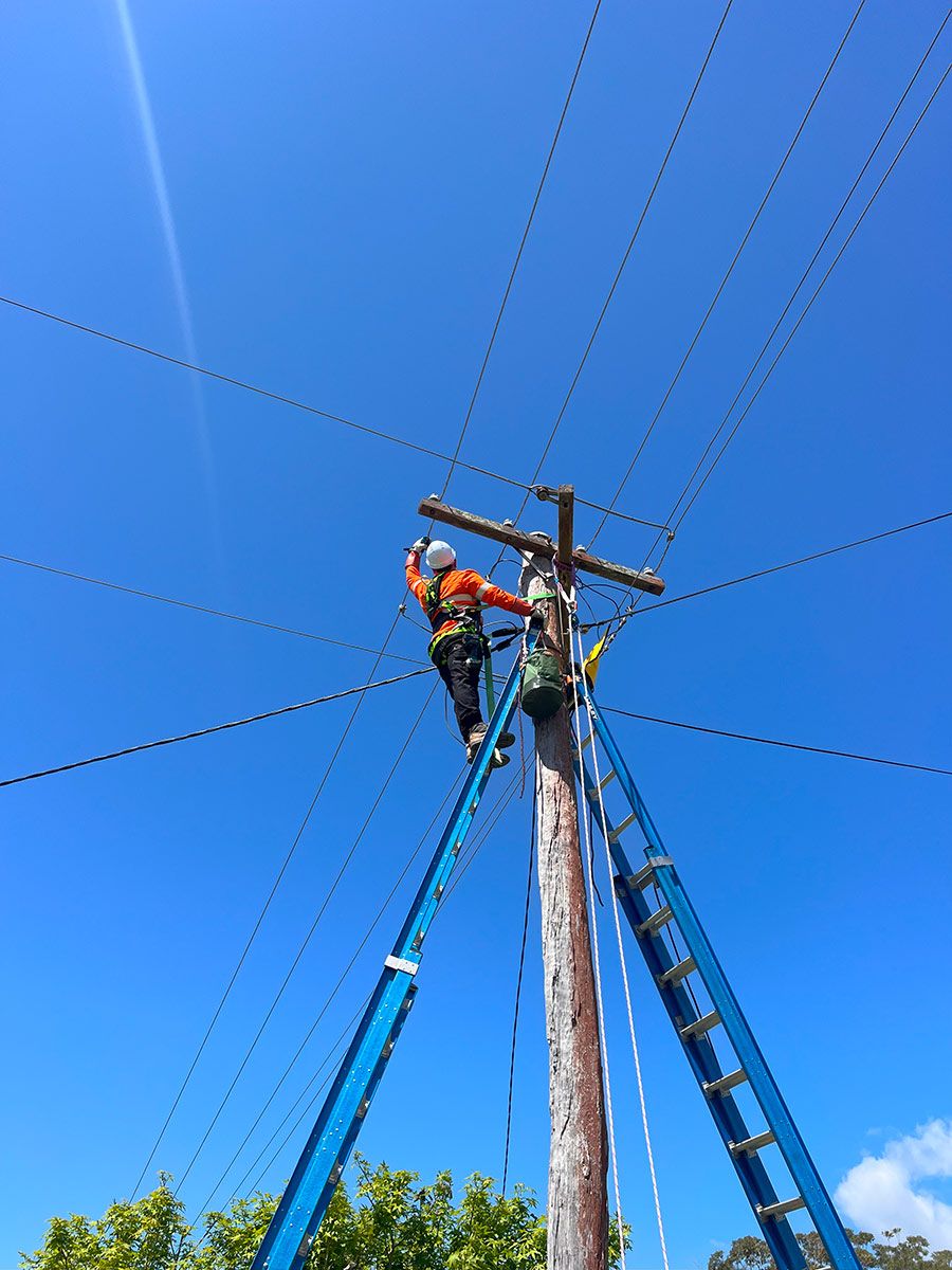 A Worker in Safety Gear is Climbing a Utility Pole — JMB Electrical Services In Port Kembla, NSW