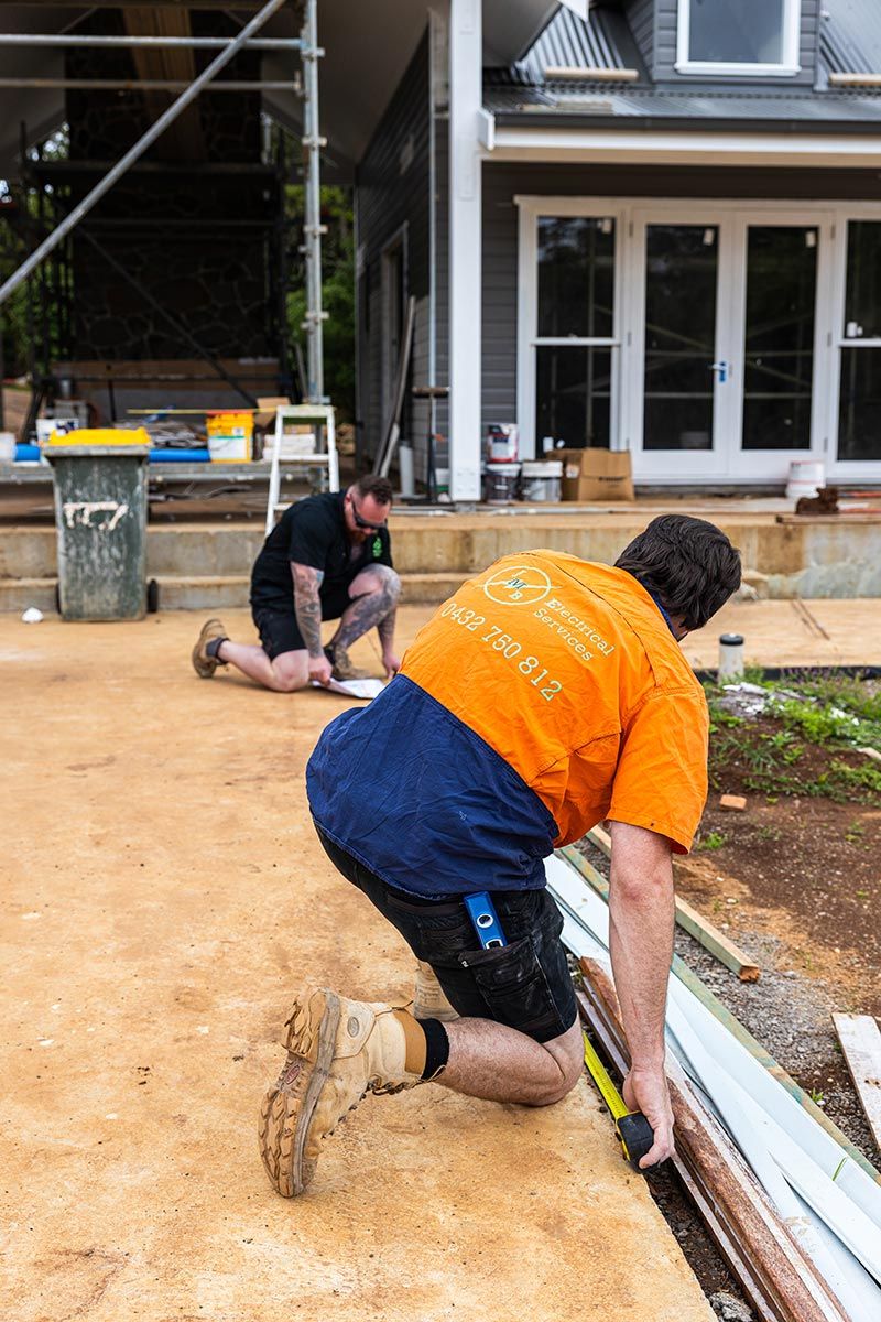 Two Construction Workers Kneel on a Partially Finished House Site — JMB Electrical Services In Port Kembla, NSW