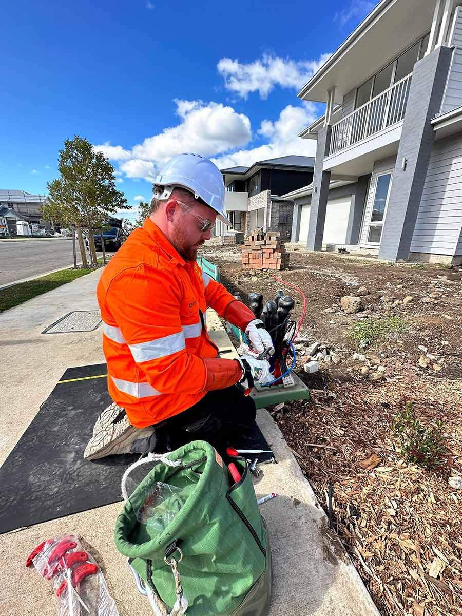 Man Kneels on a Sidewalk, Working With Cables — JMB Electrical Services In Port Kembla, NSW