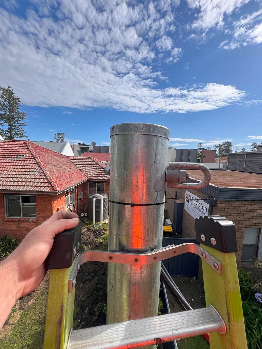 A Hand Grips a Ladder Beside a Metal Chimney — JMB Electrical Services In Port Kembla, NSW