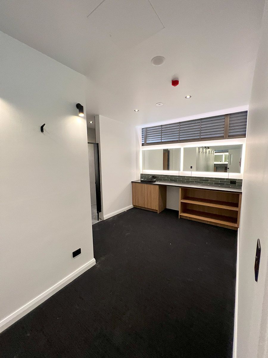 A Modern Room With White Walls, Black Carpet, and a Wooden Cabinet — JMB Electrical Services In Port Kembla, NSW