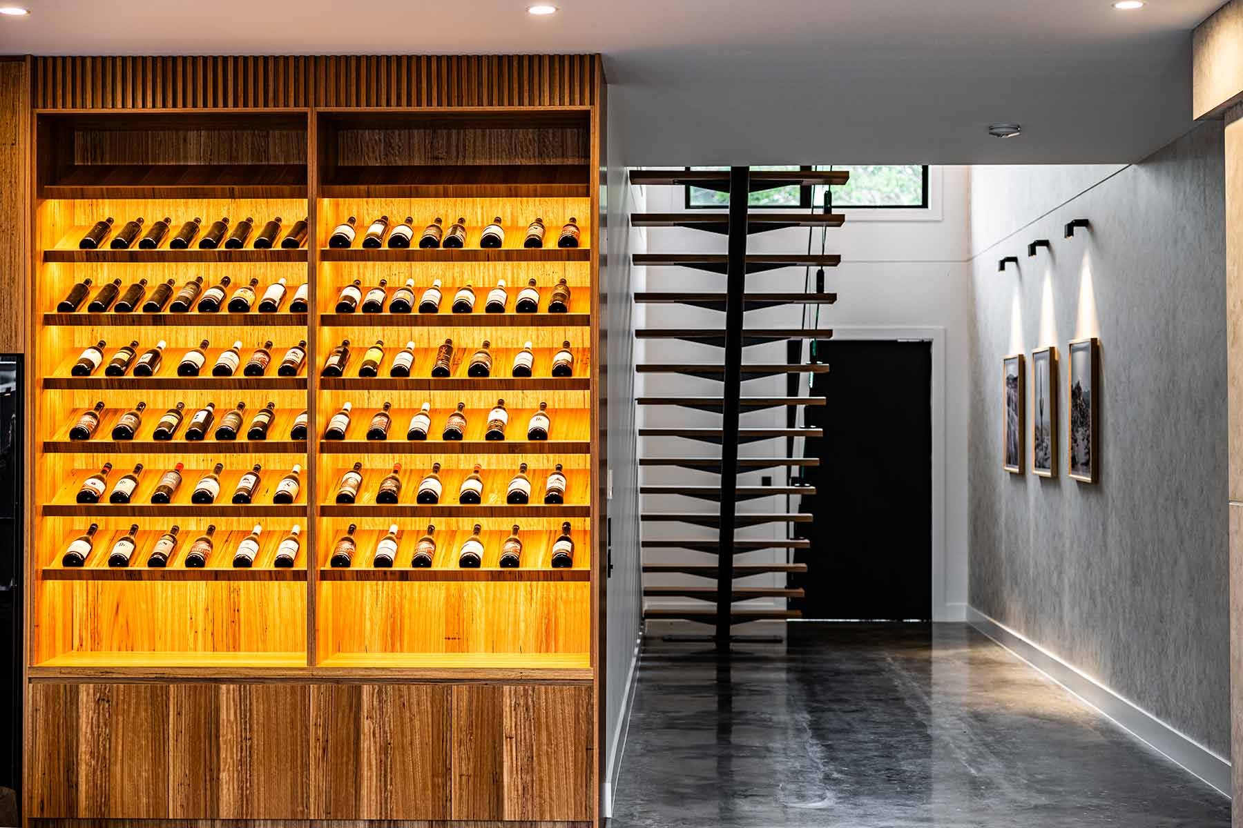 A Wooden Wine Rack Filled With Bottles and a Sleek Spiral Staircase — JMB Electrical Services In Port Kembla, NSW