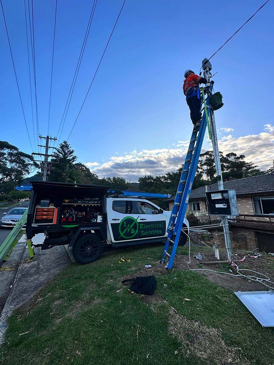 A Worker in a Safety Harness Stands on a Blue Ladder — JMB Electrical Services In Port Kembla, NSW