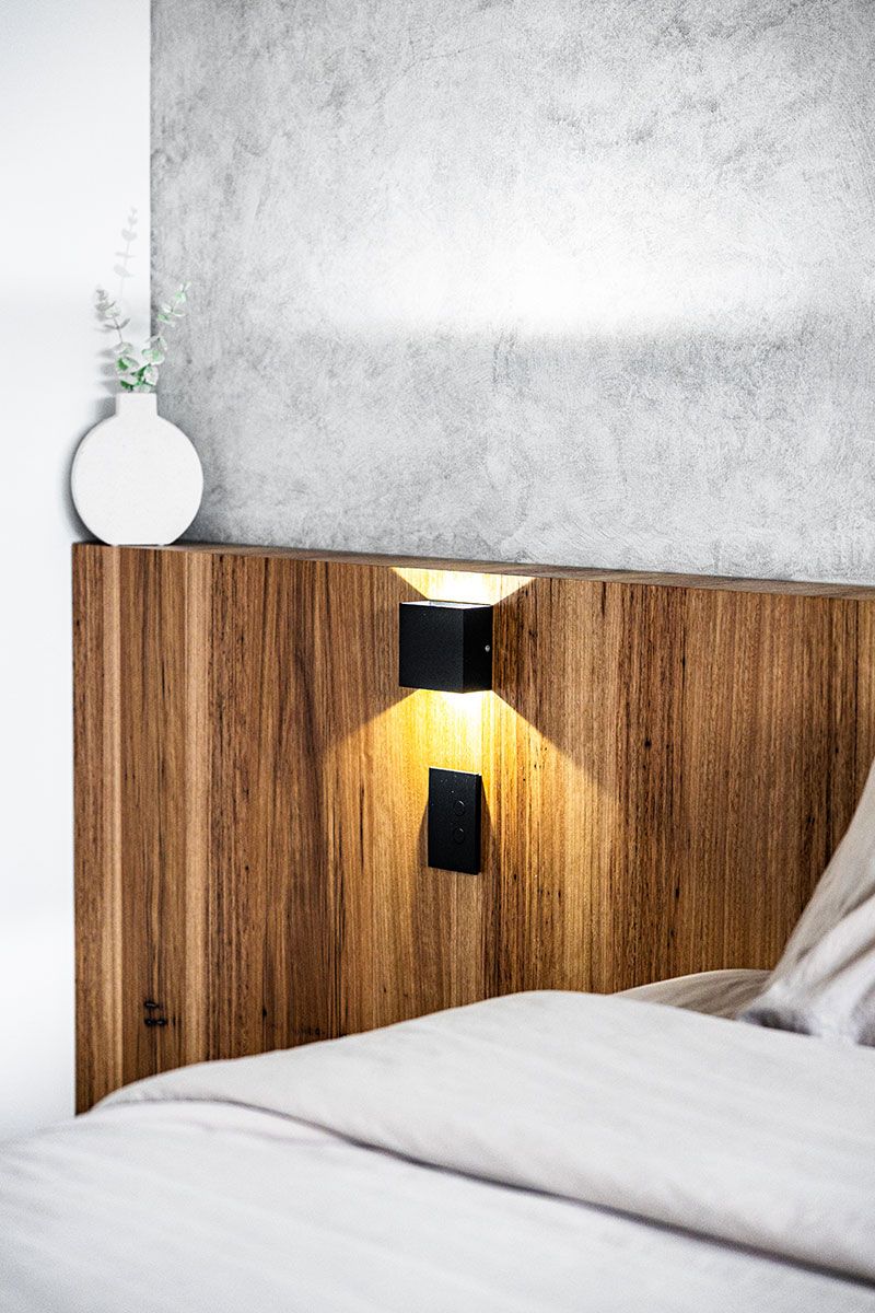Bedroom With a Textured Grey Wall and Sleek Wood Headboard — JMB Electrical Services In Port Kembla, NSW