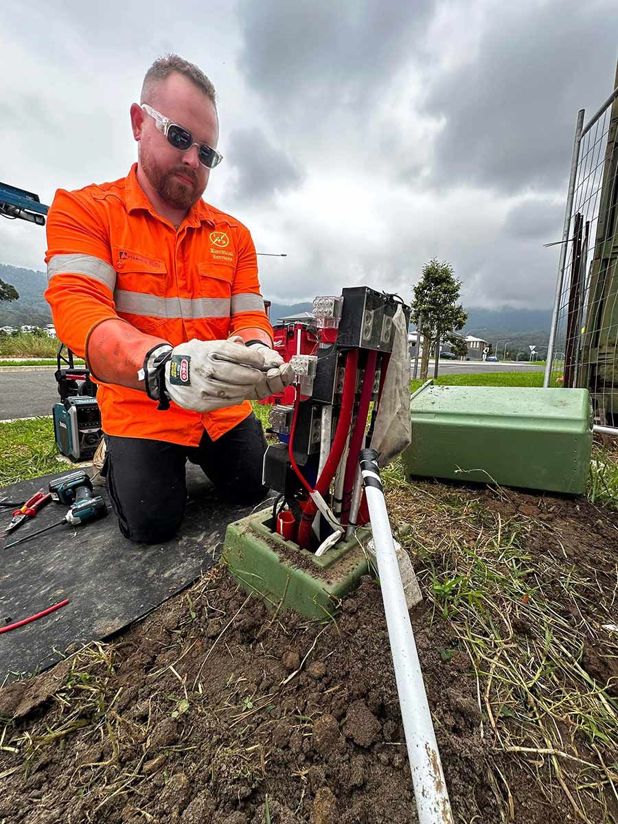 A Person in an Orange Safety Uniform Working on Electrical Equipment — JMB Electrical Services In Port Kembla, NSW