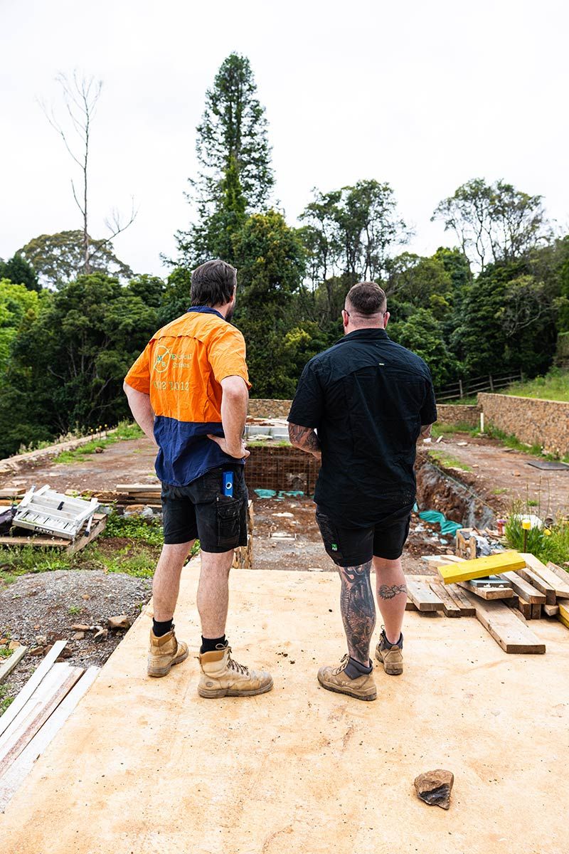 Two Men in Work Clothes Stand on a Construction Site — JMB Electrical Services In Port Kembla, NSW