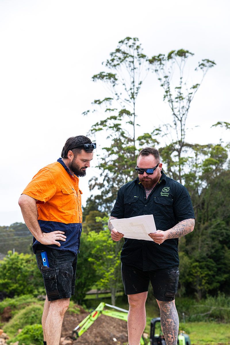 Two Men in Workwear Examine Blueprints Outdoors — JMB Electrical Services In Port Kembla, NSW