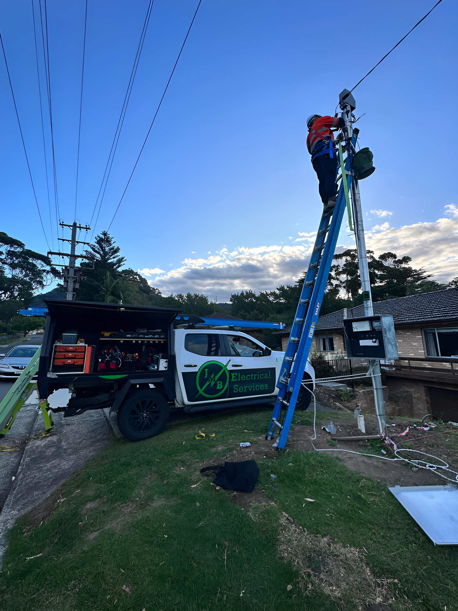 An Electrician Stands on a Blue Ladder — JMB Electrical Services In Port Kembla, NSW