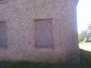 A brick building with two windows that are boarded up.