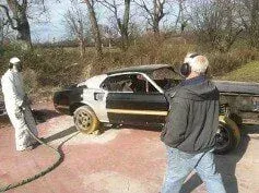 A man is standing next to a car that is being painted.