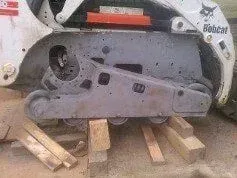 A bobcat tractor is sitting on top of a pile of wood.