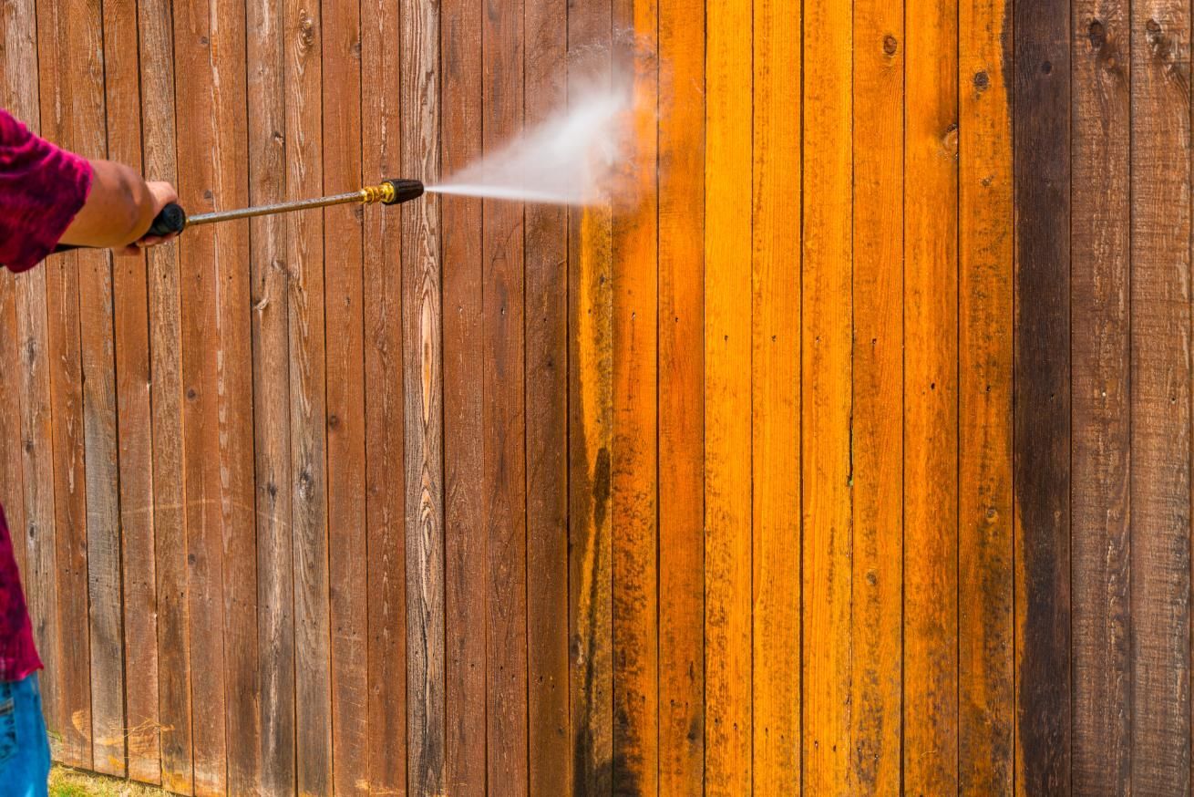 A man is using a high pressure washer to clean a wooden fence.