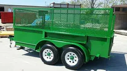 A green trailer with white wheels is parked on the side of the road.