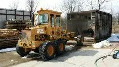 A yellow tractor is parked next to a trailer.