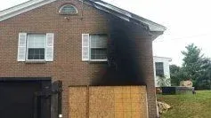 A brick house with a black roof and a wooden fence in front of it.