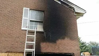 A ladder is sitting on the side of a brick building next to a window.