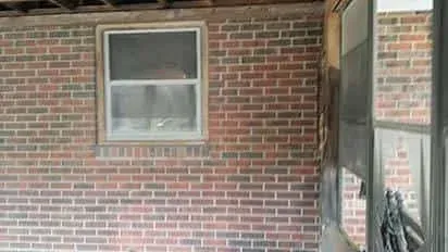 A brick wall with a window and a screen door.