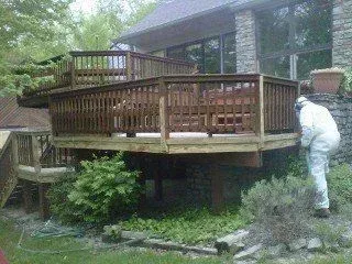 A man in a white suit is standing on a wooden deck in front of a house.