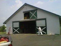 A man is standing in front of a barn with its doors open.