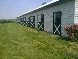 A row of horse barns are lined up in a grassy field.