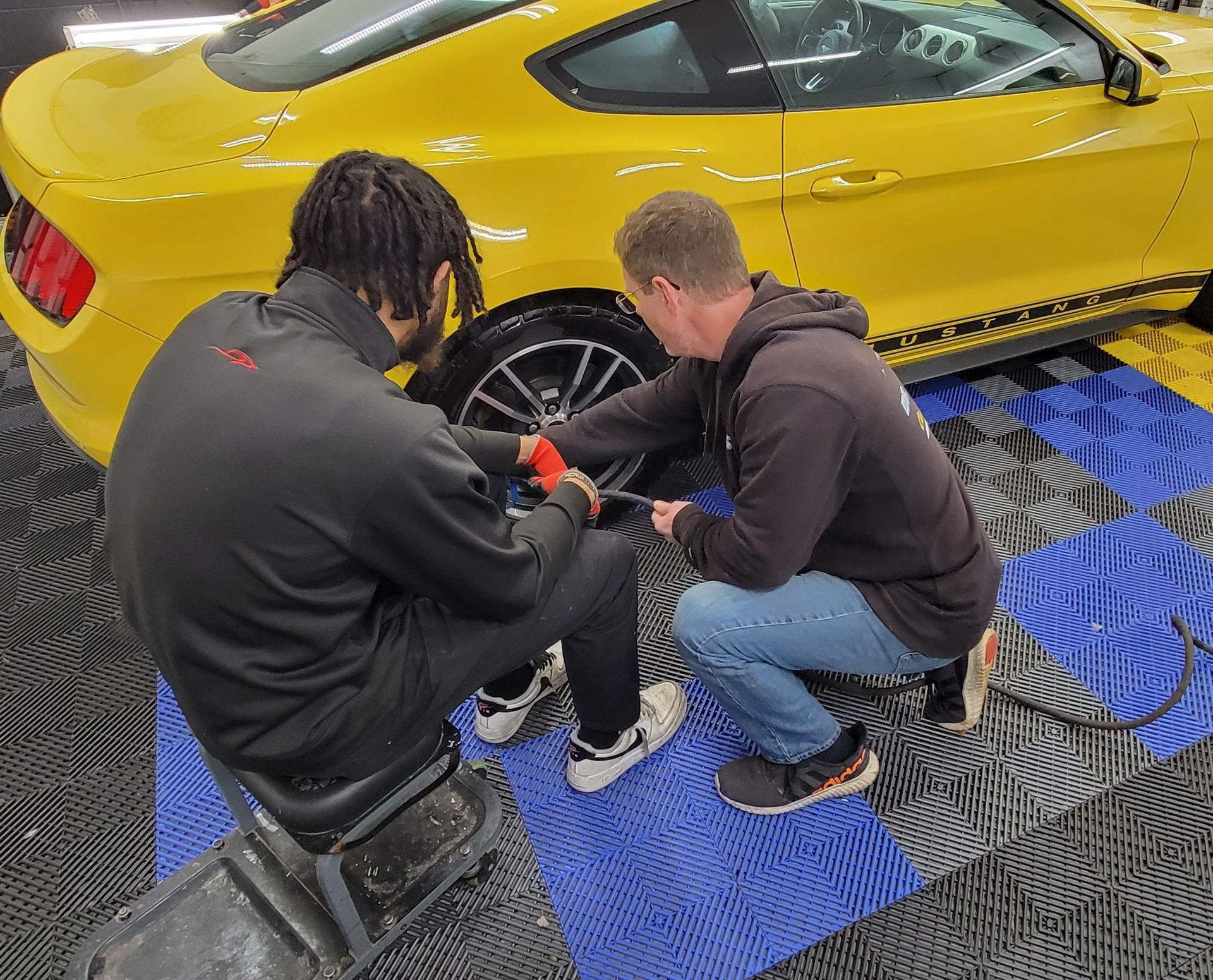 Two men are learning auto detailing techniques on a beautiful yellow, ford mustang. 