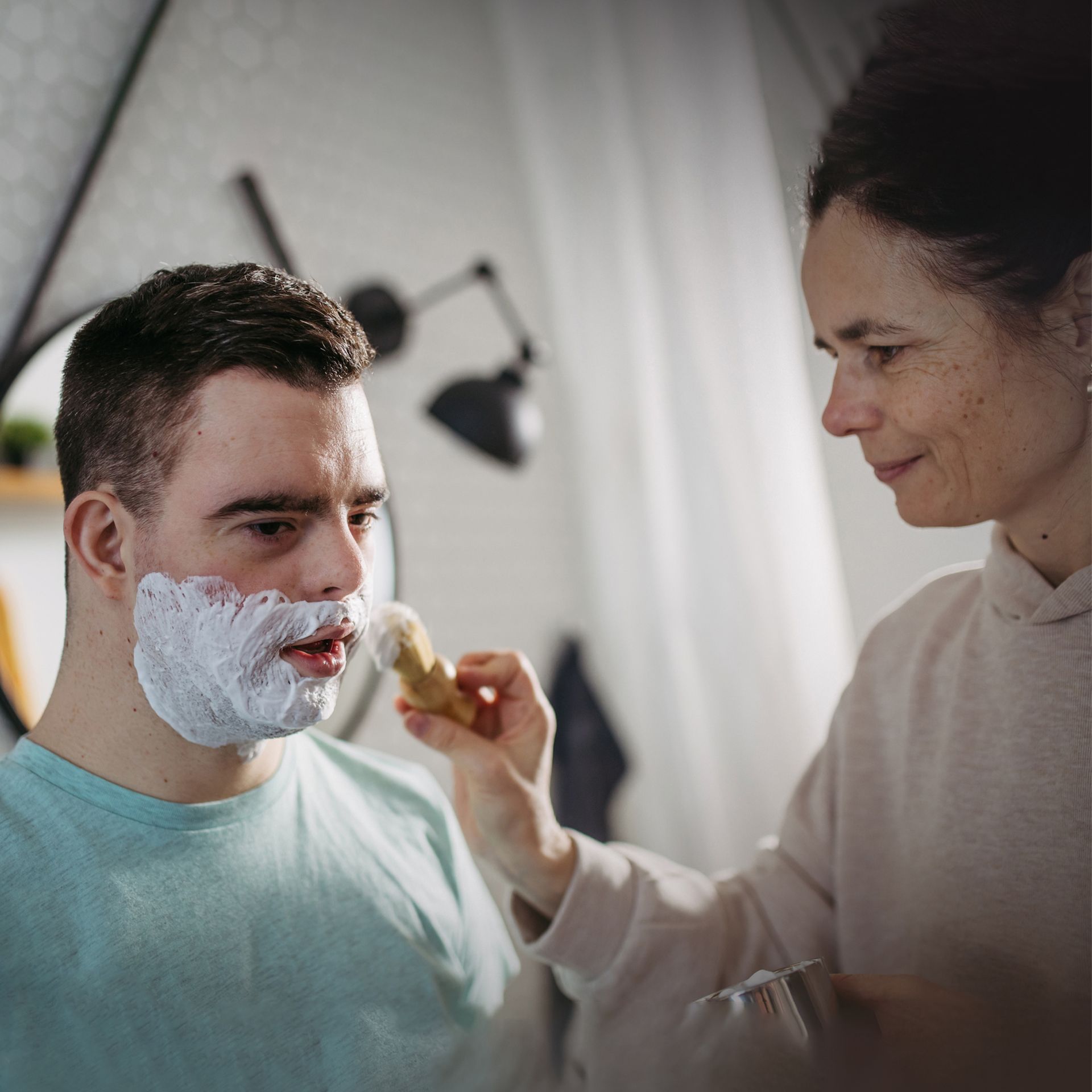 A woman is shaving a man's face with a brush.