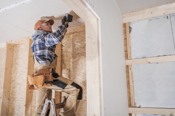 Worker on a ladder installing drywall in an unfinished room
