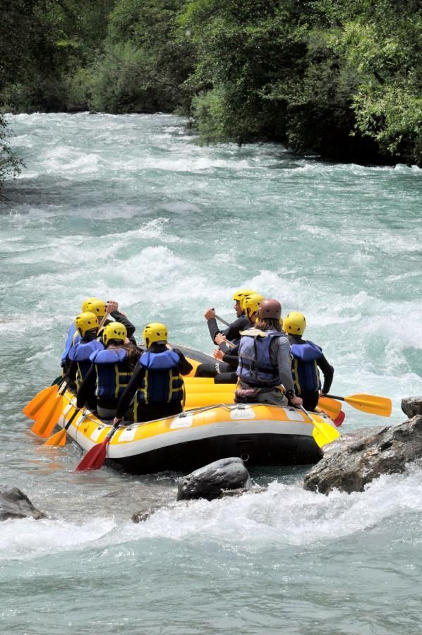 Nine people wearing protective helmets and safety vests rafting in whitewater rapids.