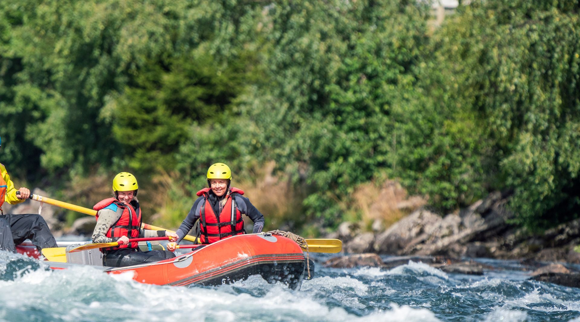 People in life vests and helmets rafting down a river with white water.