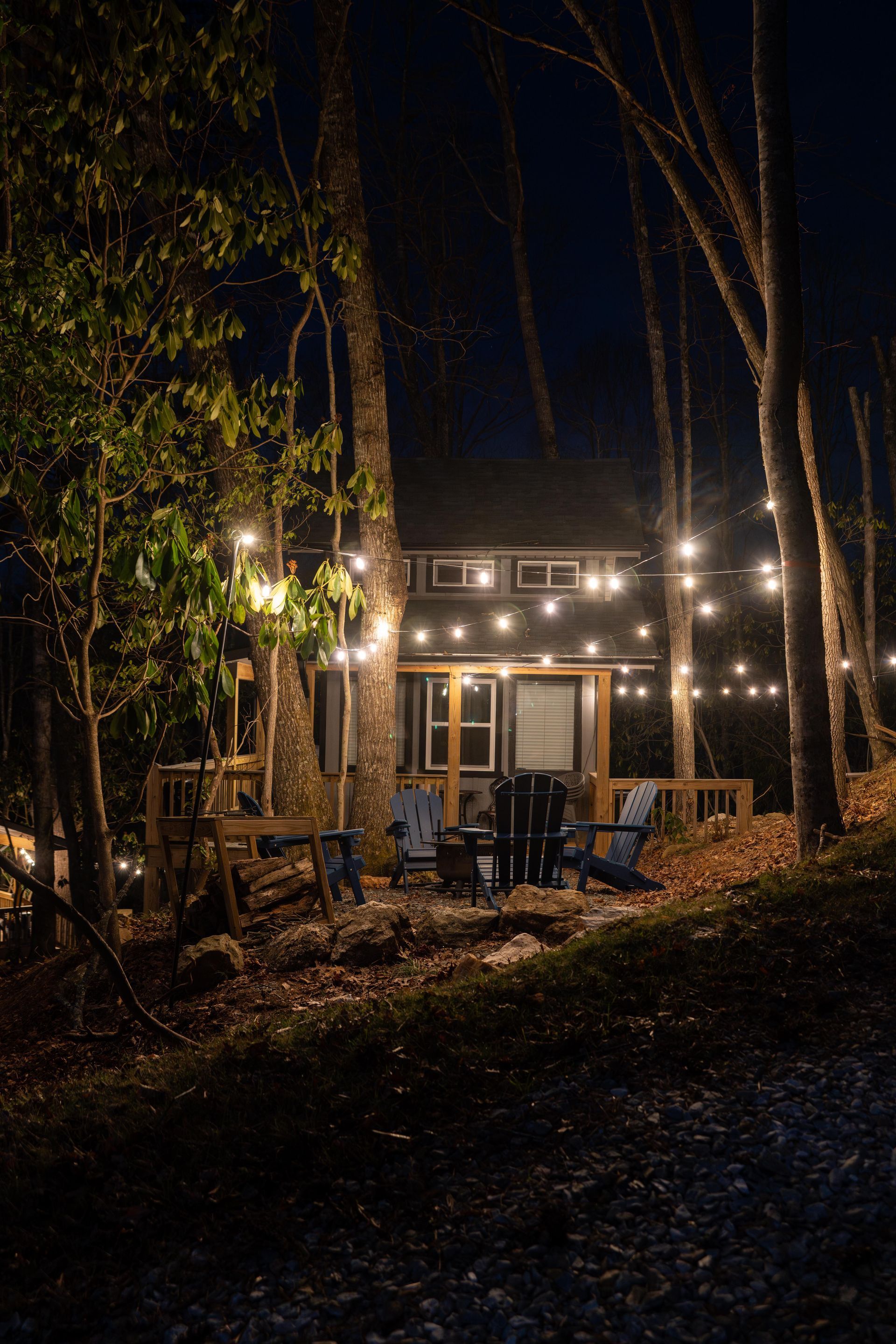 Adirondack chairs surrounding a fire pit under string lights in front of a tiny cabin.