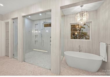 Modern bathroom with a glass shower, soaking tub, and crystal chandelier.