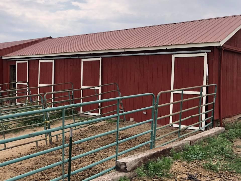 A red barn with white doors is surrounded by a green fence.