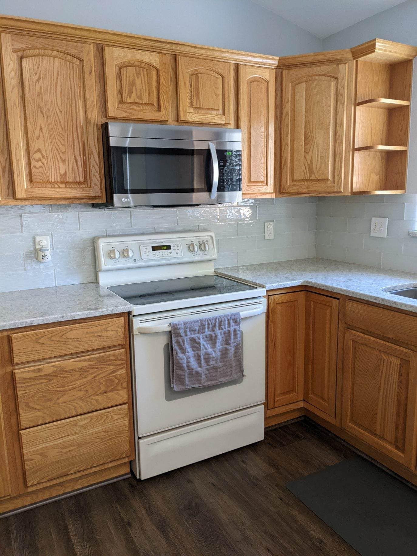A kitchen with wooden cabinets , a stove , microwave and sink.