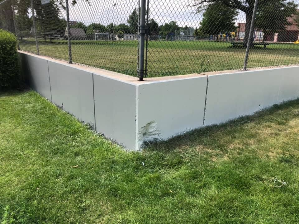 A white fence surrounds a baseball field in a park.