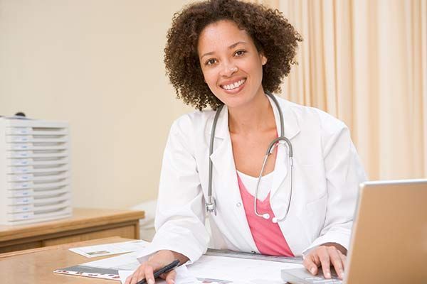 A female doctor is sitting at a desk with a laptop computer.