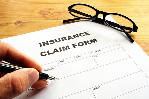 A person is filling out an insurance claim form with a pen.