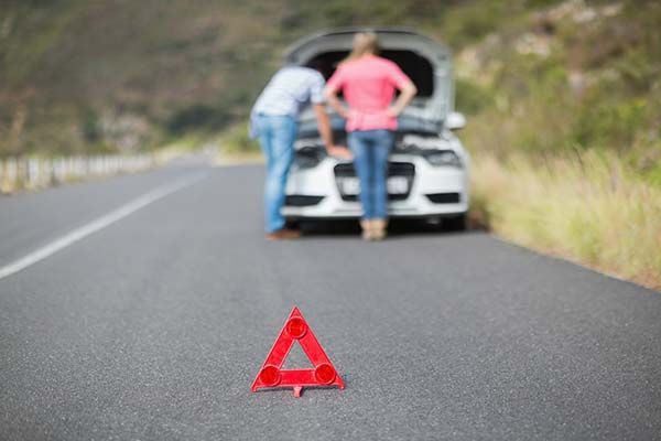 A man and a woman are looking under the hood of a broken down car.