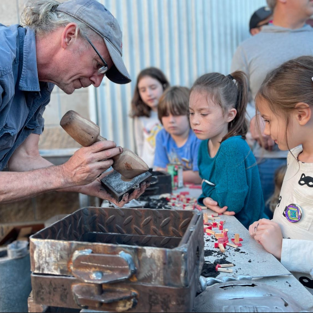 Man carving wood at a table while children watch during a hands-on workshop