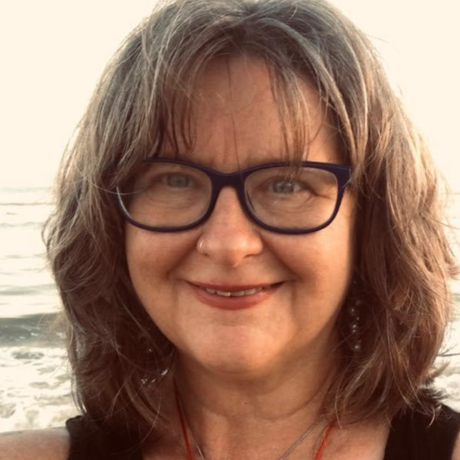 Smiling woman with glasses and shoulder-length brown hair at the beach
