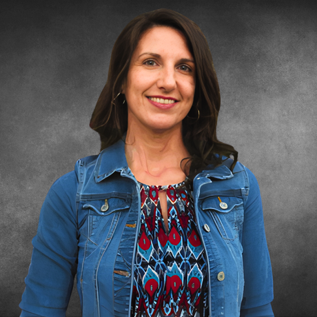 Smiling woman in a denim jacket and patterned top against a gray studio backdrop