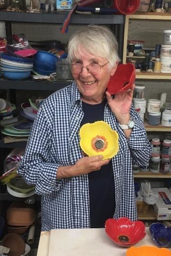 Smiling woman in a shop holding a yellow flower-shaped bowl, with shelves of pottery behind her