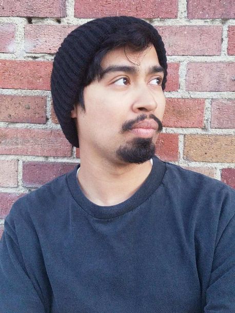 Person in a black beanie and gray shirt looking to the side against a brick wall