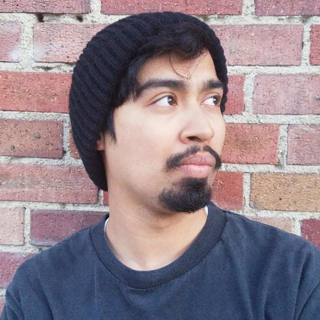 Person in a black beanie and gray shirt looking to the side against a brick wall