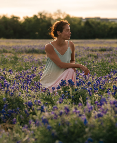 Woman sitting in a purple wildflower field at sunset, wearing a white dress and looking to the side