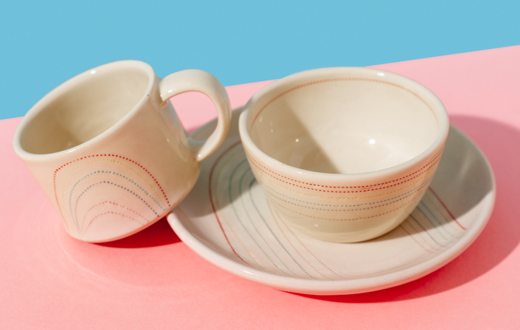 Cream-colored cup and bowl with matching plate on a pink background.