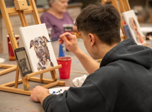 Art students painting at easels in a studio, with one focused on a portrait sketch.