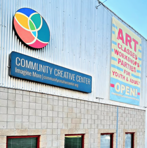 Community Creative Center sign on a building with colorful art classes, workshops, and youth/adult open notice.