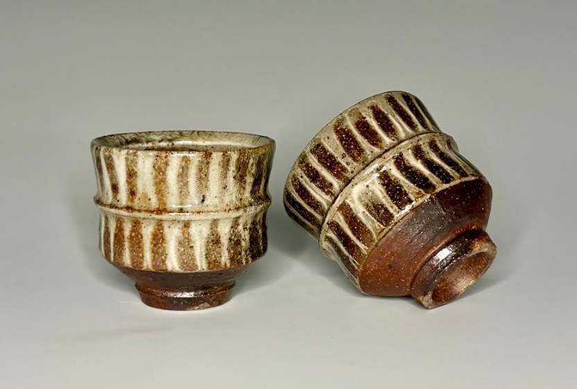 Two small striped ceramic cups, one upright and one tilted on a light background